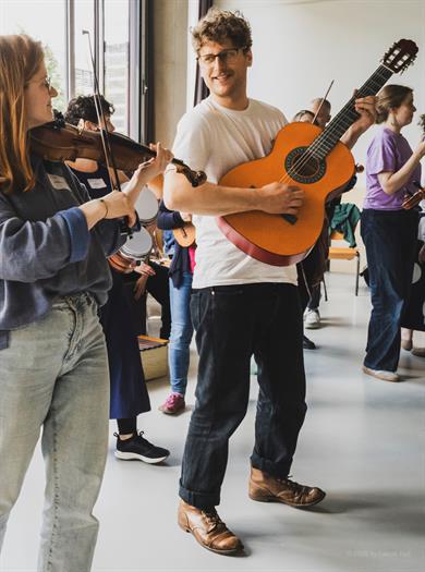 Ein Bild vom nationalen Community Music Netzwerktreffen auf dem musizierende Menschen in einer Gruppe zu sehen sind. 